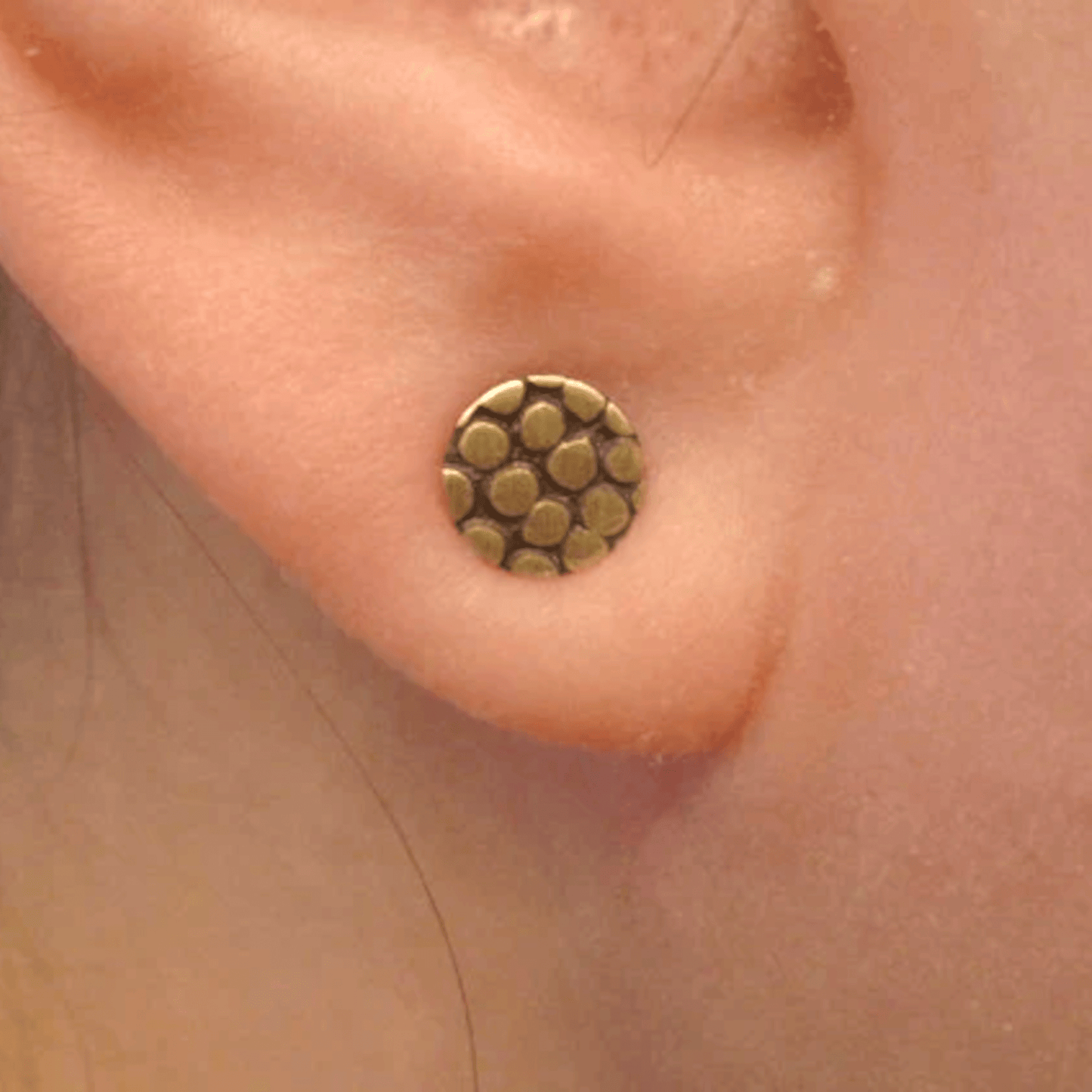 Close-up of the Pebble Texture Brass Circle Stud Earrings worn on an ear, showcasing their organic texture and size