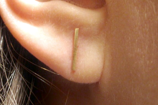 Gold Colored Brass bar earring worn on a person's ear