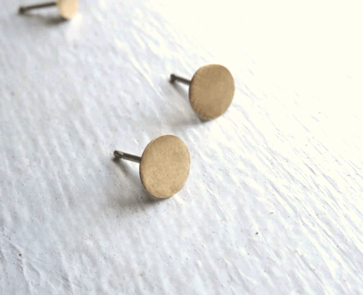 Close-up of 5mm brass circle stud earrings with matte finish and sterling silver backs.