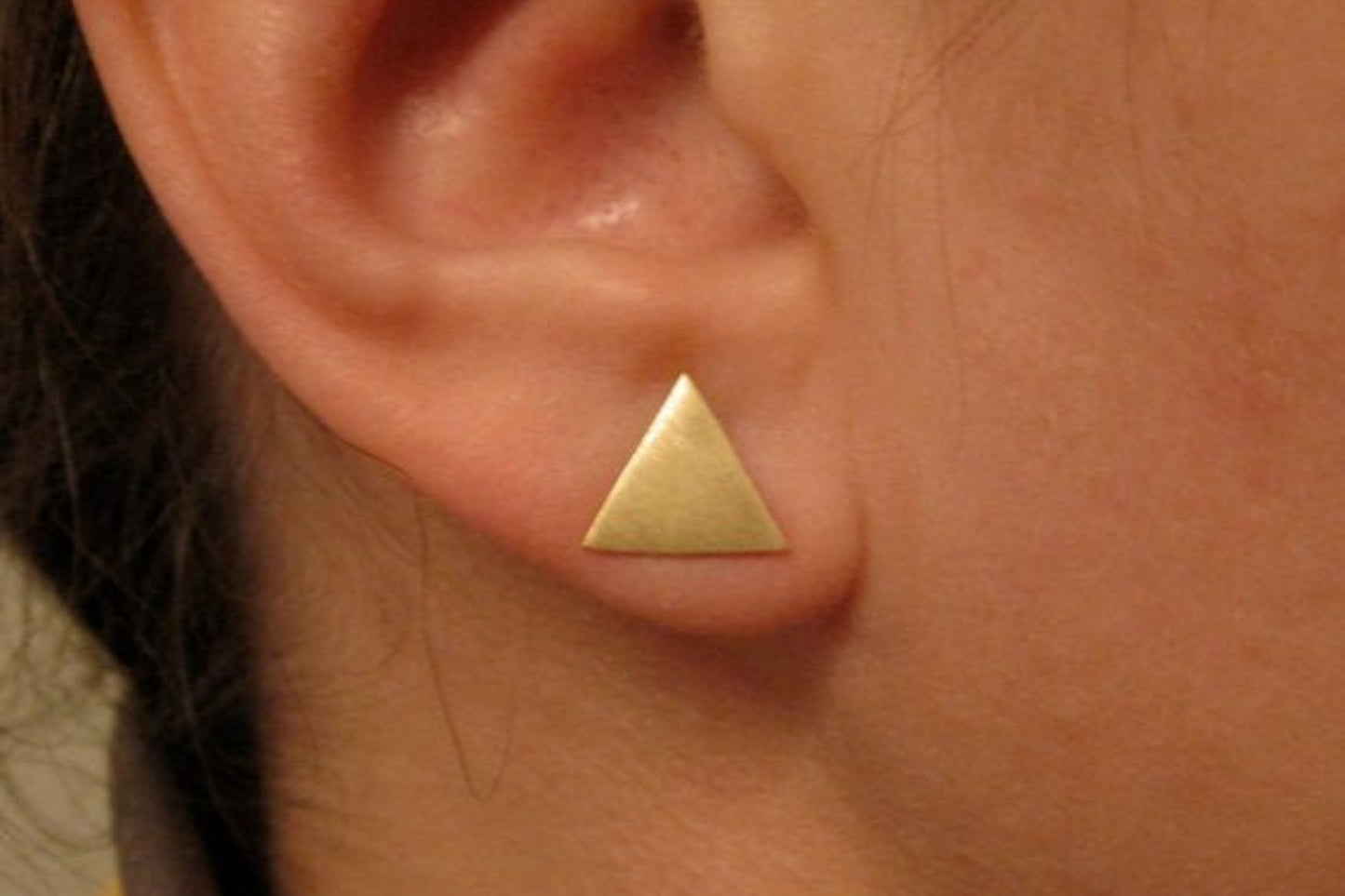 Gold triangle earring worn on an ear