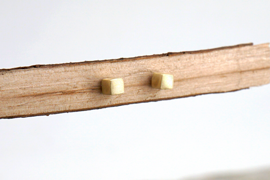 Two gold square stud earrings on a wooden stick against a white background
