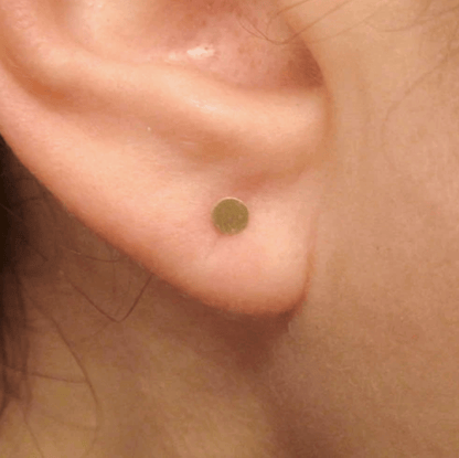 Tiny 3mm brass stud earring worn on an ear