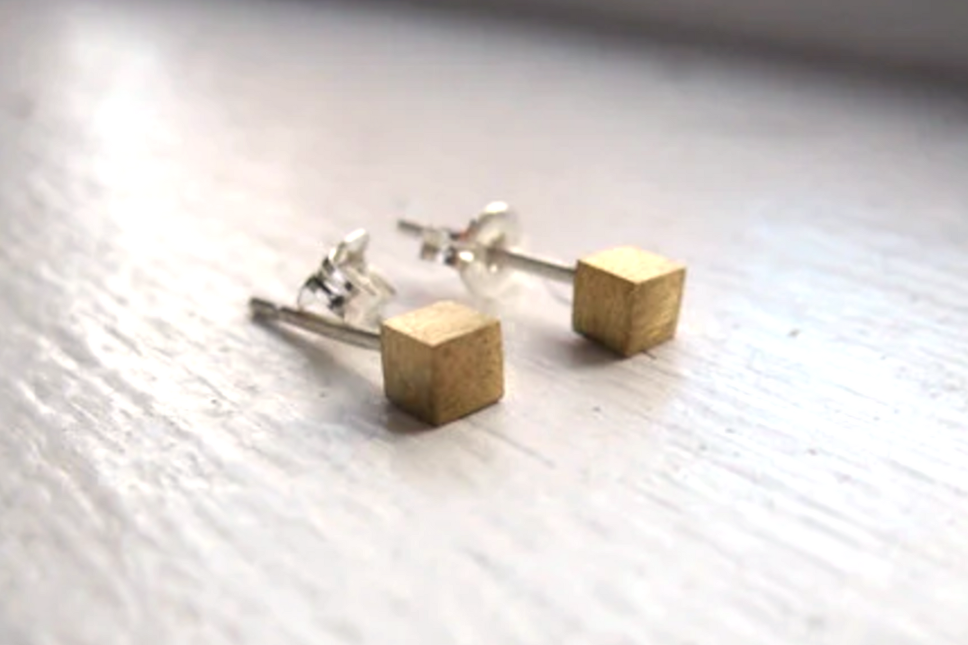 Gold cube stud earrings on a light wooden surface