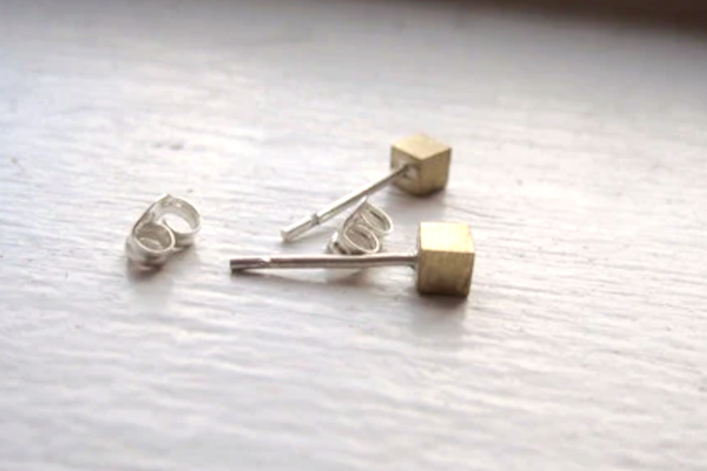 Pair of gold and silver cube-shaped earrings on a textured white surface.