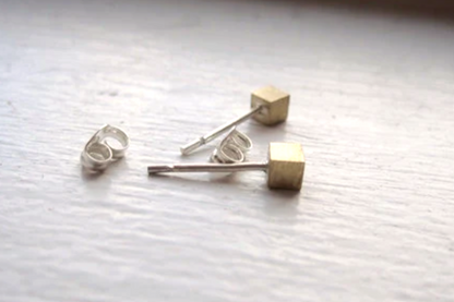 Pair of gold and silver cube-shaped earrings on a textured white surface.