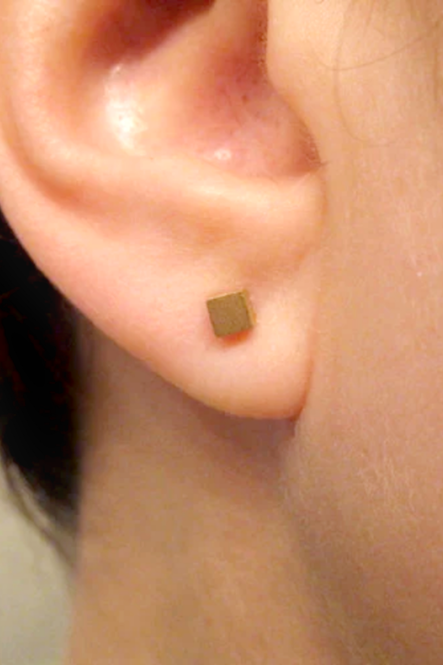 Gold square stud earring on a person's ear