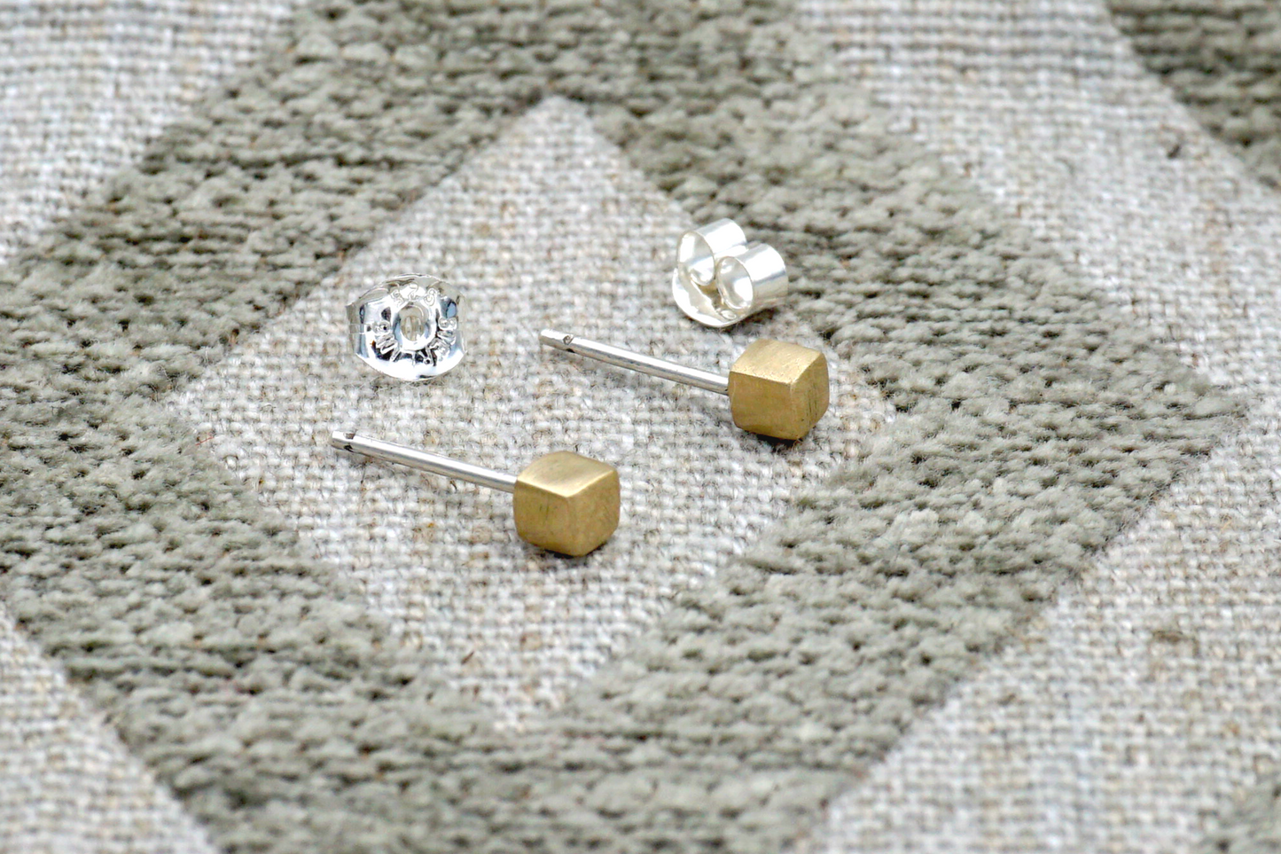Gold and silver stud earrings on a textured fabric surface