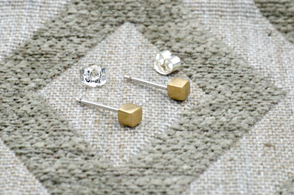Gold and silver stud earrings on a textured fabric surface